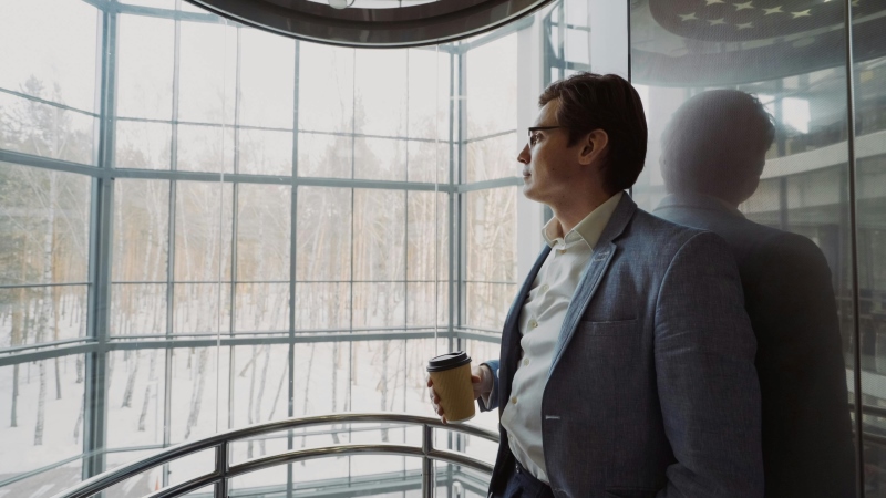 Empresário observando a cidade pela janela refletindo sobre decisões estratégicas do negócio