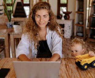 Mãe trabalhando no notebook enquanto a filho observa em ambiente familiar acolhedor