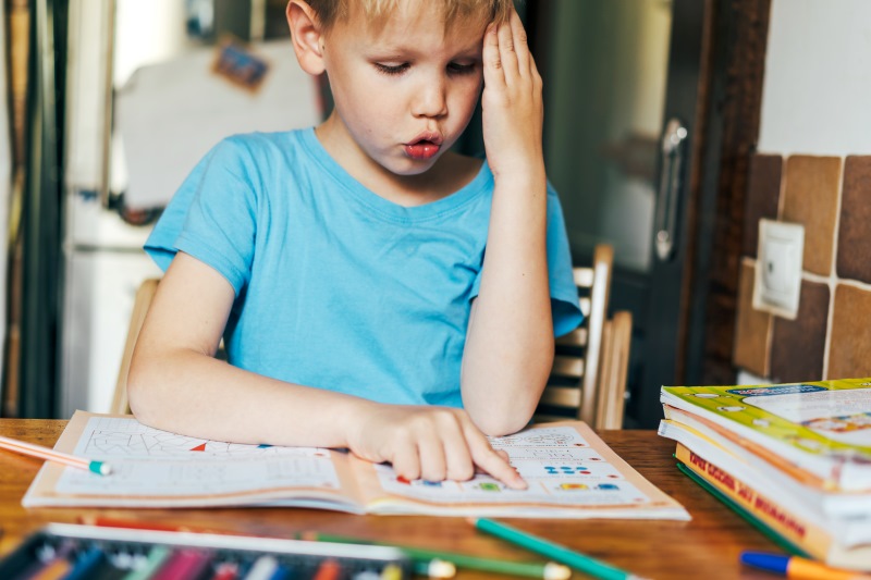 Menino concentrado em livro de quebra-cabeças sobre uma mesa de madeira e o Bilinguismo infantil
