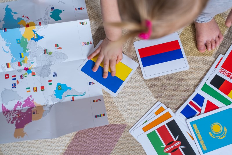 Criança estudando bandeiras de países diante de um mapa-múndi caracteriza o Bilinguismo infantil