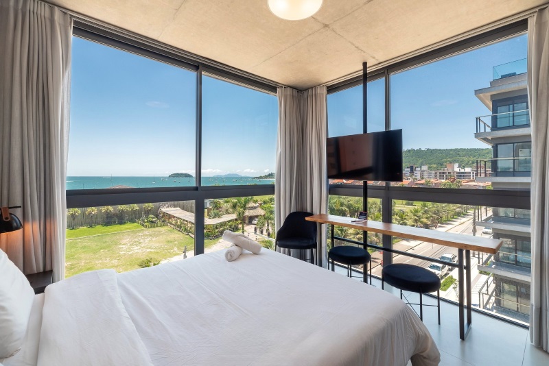 Suíte com cama de casal e grandes janelas com vista para o exterior promove experiencias ao turismo esportivo