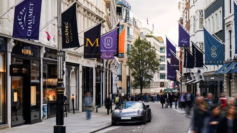 Rua com lojas de luxo dos dois lados e bandeiras do Main Streets Across the World