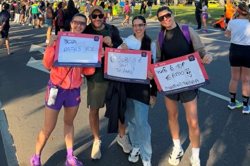 Três corredoras do turismo esportivo seguram cartazes da Seazone durante uma ação relacionada à corrida