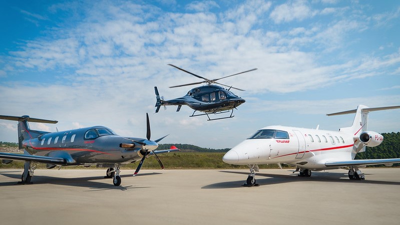 Dois aviões Pilatus no solo com helicóptero se aproximando no angar da Amaro Aviation