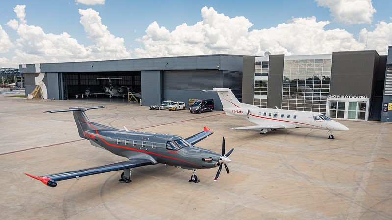 Avião Pilatus monomotor e jato executivo lado a lado próximo a um hangar