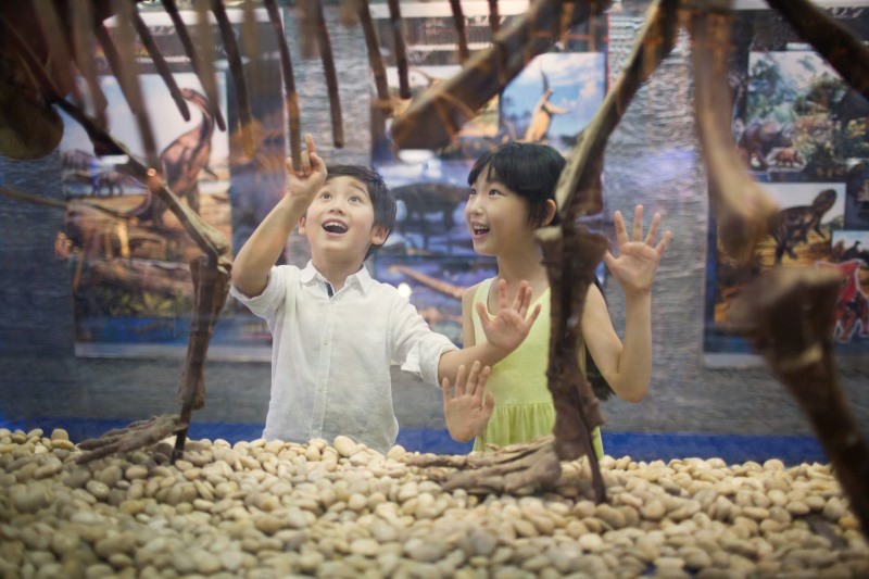 Crianças explorando com entusiasmo um esqueleto de dinossauro em museu
