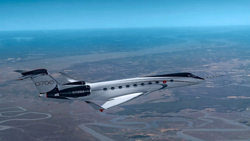 Gulfstream G700 voando sobre uma cidade sob céu azul