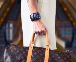 Mulher de branco usando relógio de pulso e segurando bolsa Louis Vuitton