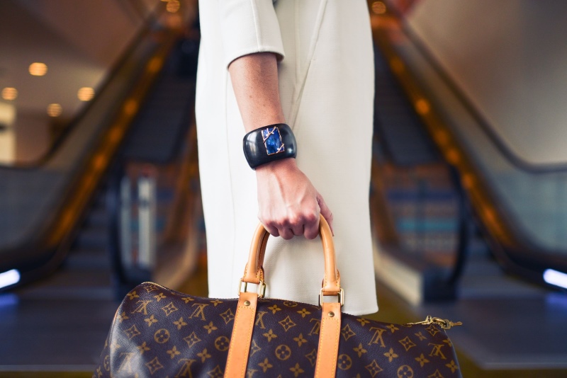 Mulher de branco usando relógio de pulso e segurando bolsa Louis Vuitton denota Riqueza e qualidade de vida