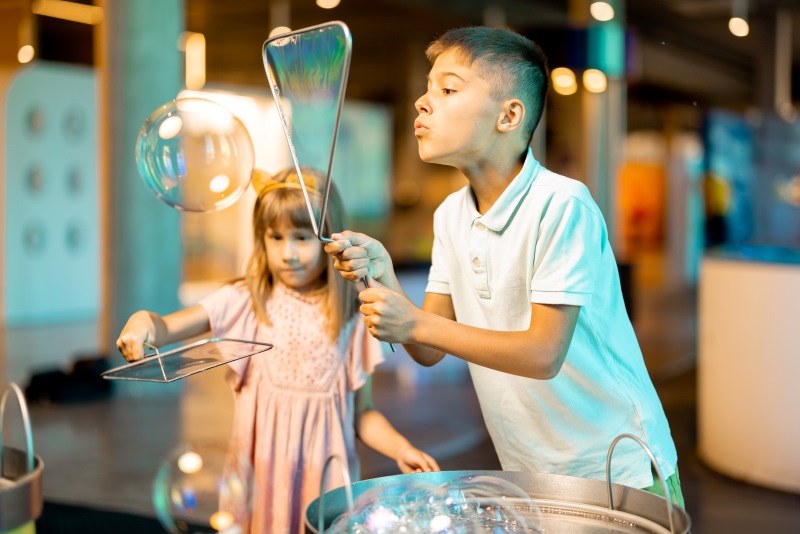 Crianças brincando de fazer bolhas dentro de um ambiente fechado