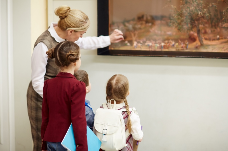 Crianças observando uma obra de arte em um museu com uma professora.
