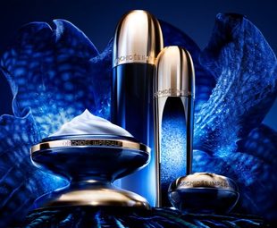 Produtos Guerlain Orchidée Impériale Concentrado da Longevidade em diferentes embalagens, sobre fundo azul