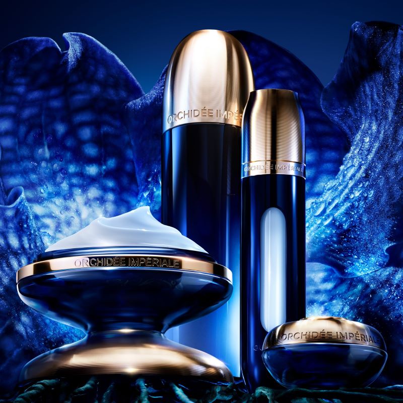 Diferentes embalagens da linha Guerlain Orchidée Impériale em composição sobre fundo azul