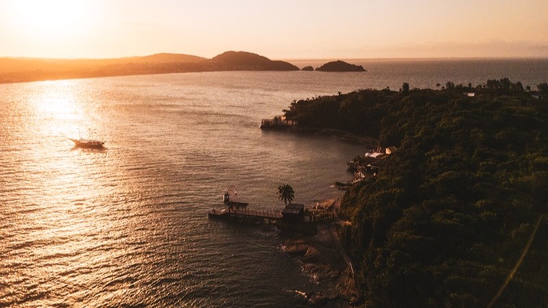 Vista aérea da Ilha Rasa ao pôr do sol, com o mar e parte da estrutura do Nas Rocas Club