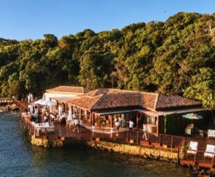 Vista aérea do Nas Rocas Club na Ilha Rasa, em Búzios, com áreas de convivência e guarda-sóis