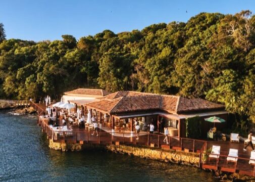 Vista aérea do Nas Rocas Club na Ilha Rasa, em Búzios, com áreas de convivência e guarda-sóis