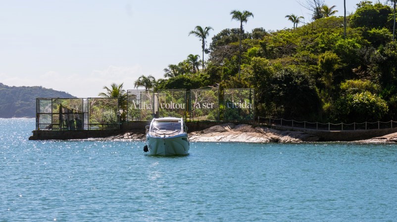 Lancha diante da costa da Ilha Rasa, vegetação abundante ao fundo
