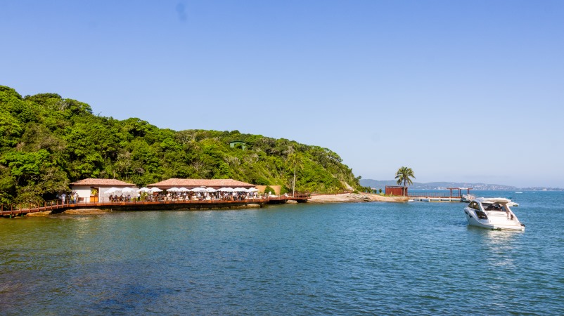 Pier com guarda-sóis, vegetação da Ilha Rasa e uma lancha no mar