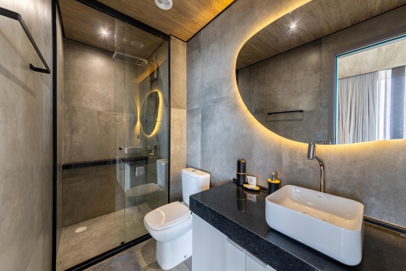 Banheiro do New Time com box, paredes de concreto e espelho iluminado