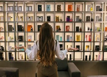 Pessoa observando uma prateleira repleta de perfumes em referência ao burnout olfativo e excesso de estímulos na perfumaria