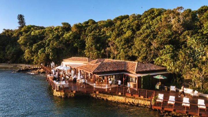 Vista aérea do Nas Rocas Club na Ilha Rasa, em Búzios, com áreas de convivência e guarda-sóis